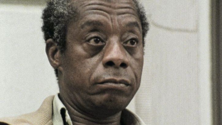 Still from the film "I Heard It through the Grapevine" by Dick Fontaine. James Baldwin, an older man with grey-brown hair and a brown jacket, is looking past the camera on the right side with an unimpressed expression.