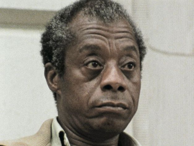 Filmstill aus dem Film "I Heard It through the Grapevine" von Dick Fontaine. James Baldwin, ein älterer Mann mit grau-braunen Haaren und einer braunen Jacke, guckt unbeeindruckt rechts neben der Kamera vorbei.