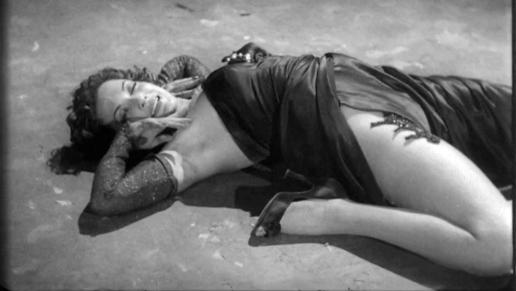 Film still from MÁS FUERTE QUE EL AMOR: A woman in an evening dress lies strangely contorted on the floor.