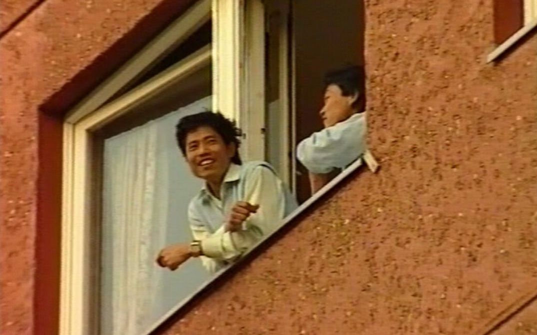 Filmstill aus BRUDERLAND: Zwei Menschen blicken aus dem geöffneten Fenster eines Hauses.