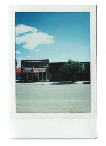 Polaroid of a street in a small town, including a building with the word “Arcade”.