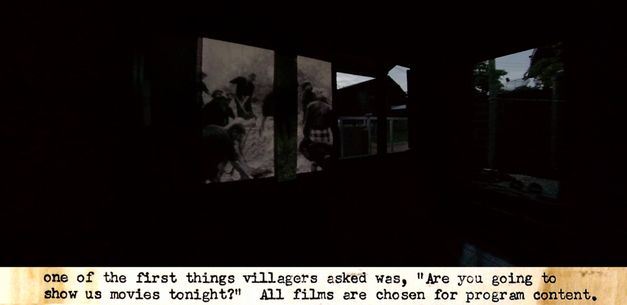 Film still from the film "Trip After" by Ukrit Sa-nguanhai. A dark room with a projected image on the wall. The captions on the image read: "one of the first things villagers asked was, 