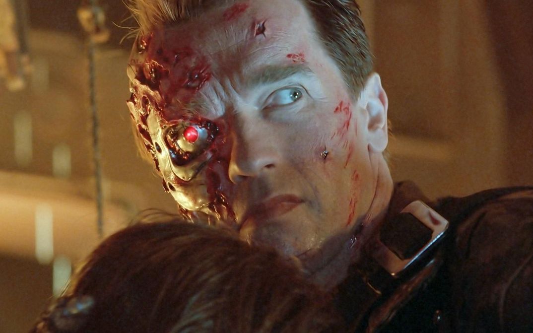 Filmstill aus TERMINATOR 2: Ein Mann mit vernarbtem, blutigen Gesicht und einem rot leuchtenden Auge schaut nach rechts.