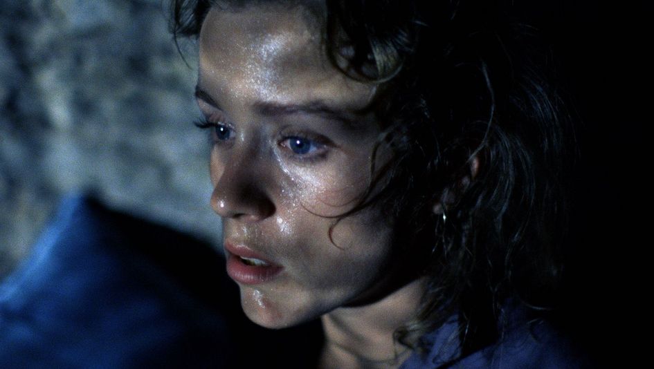 Filmstill aus BLOOD SIMPLE: Man sieht das Gesicht einer Frau im Dunkeln, sie sieht ängstlich aus.