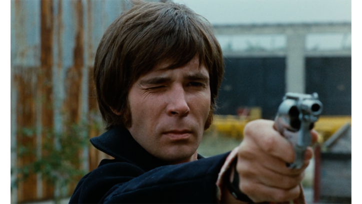 Film still from FEGEFEUER. A man aims his revolver into the distance.