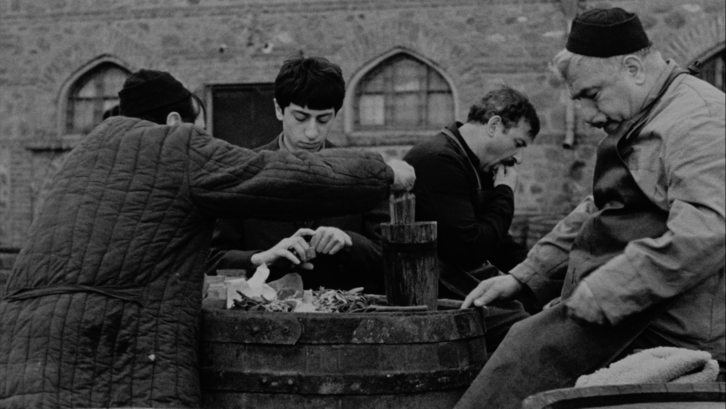 Film still from FALLING LEAVES: A few guys are standing around a wine barrel.