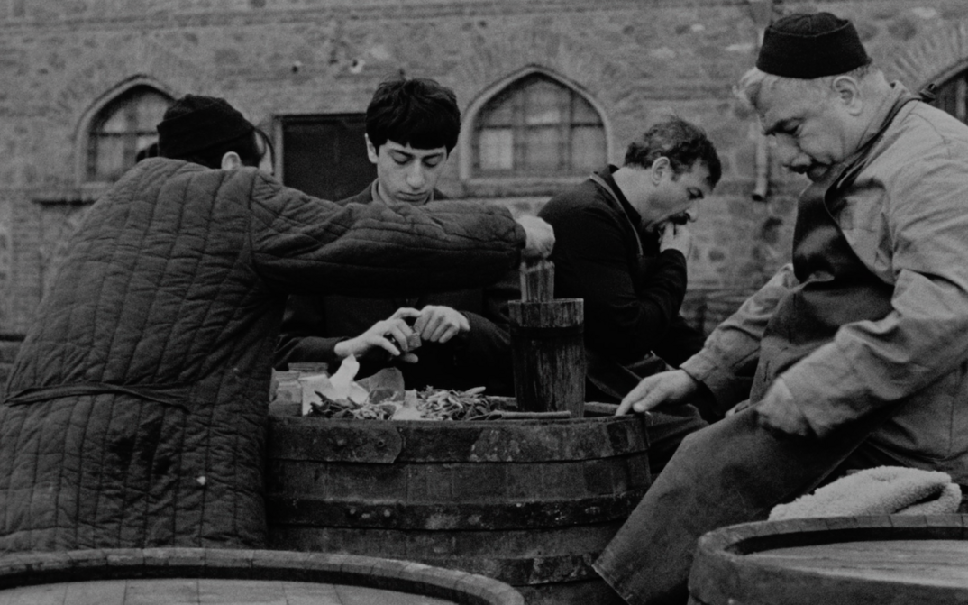 Film still from FALLING LEAVES: A few guys are standing around a wine barrel.