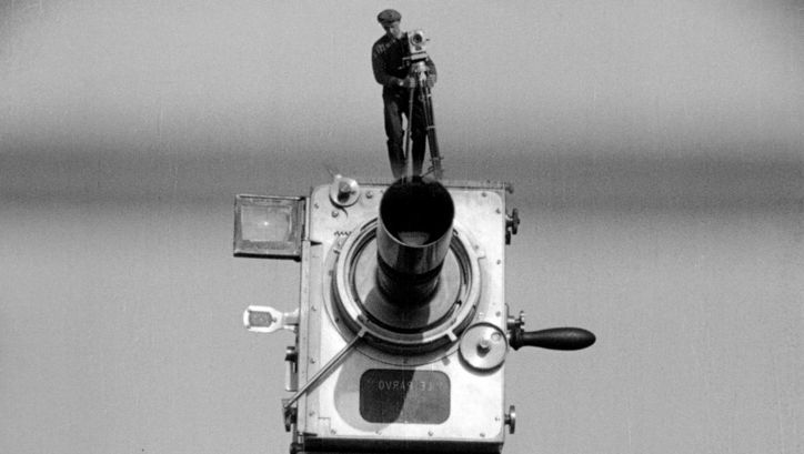 Filmstill from MANN MIT DER KAMERA: A large old camera on which a man is standing with the same camera. He looks like a miniature.