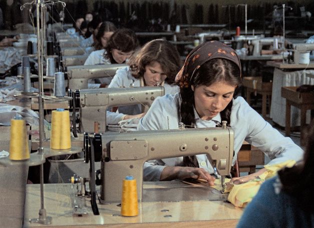 Filmstill aus „Kara Kafa“ von Korhan Yurtsever. Zu sehen ist eine Reihe von Arbeitsplätzen mit Nähmaschinen, an denen Frauen arbeiten.