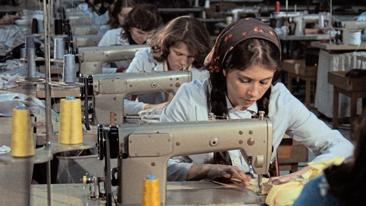 Filmstill aus „Kara Kafa“ von Korhan Yurtsever. Zu sehen ist eine Reihe von Arbeitsplätzen mit Nähmaschinen, an denen Frauen arbeiten.