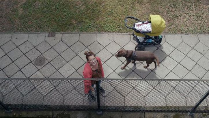 Film still from THE BALCONY MOVIE. View from a balcony on the street, a woman with a dog and stroller looks up.