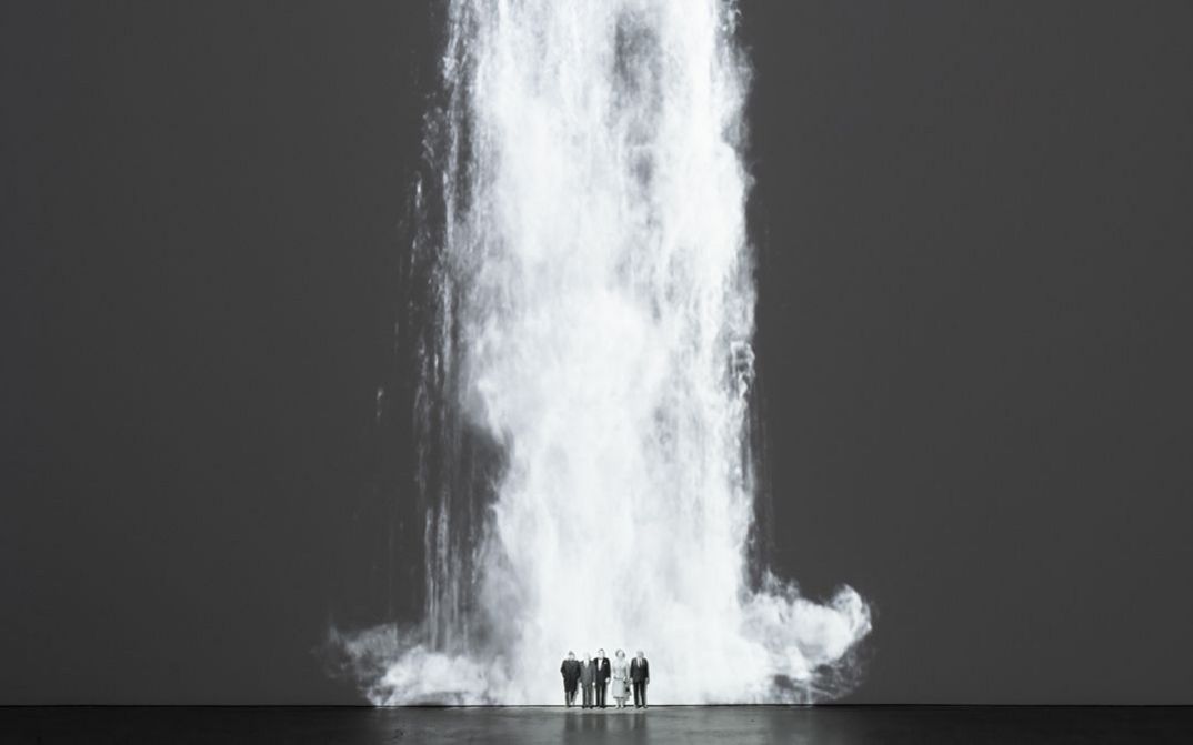 Installation view of Walid Raad’s „Comrade leader, comrade leader, how nice to see you“. A waterfall projected unto a wall; at its foot five figures standing next to each other.