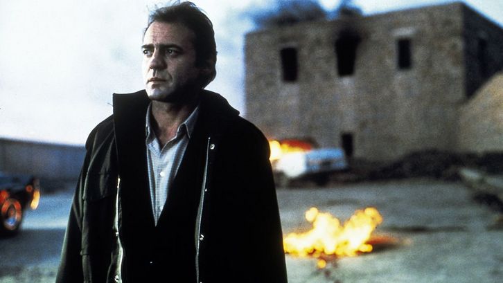 Filmstill aus DIE FÄLSCHUNG. Der Schauspieler Bruno Ganz im Vordergrund, im Hintergrund unscharf ein brennendes Haus.