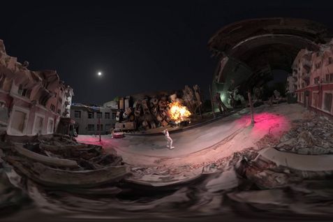 Film still from Alisa Berger’s film “RAPTURE”. This 360-degree panoramic scene is a virtual reality reconstruction of a nocturnal apocalyptic environment. The 3D modeling features partially collapsed buildings. At the center of the virtual environment, an explosion or fire can be seen. Pink/red lighting effects are projected onto the ground. A white-clothed avatar is placed in the street.