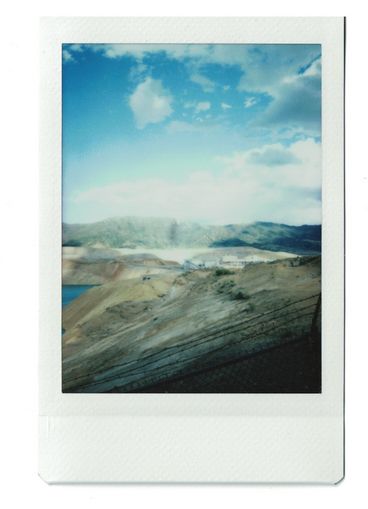 Polaroid of the bank of a reservoir, with darkened by the shadows of clouds. 