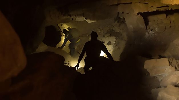 Still from the film "The Zama Zama Project" by Rosalind Morris. In an underground tunnel, you can see the silhouette of a man from behind.