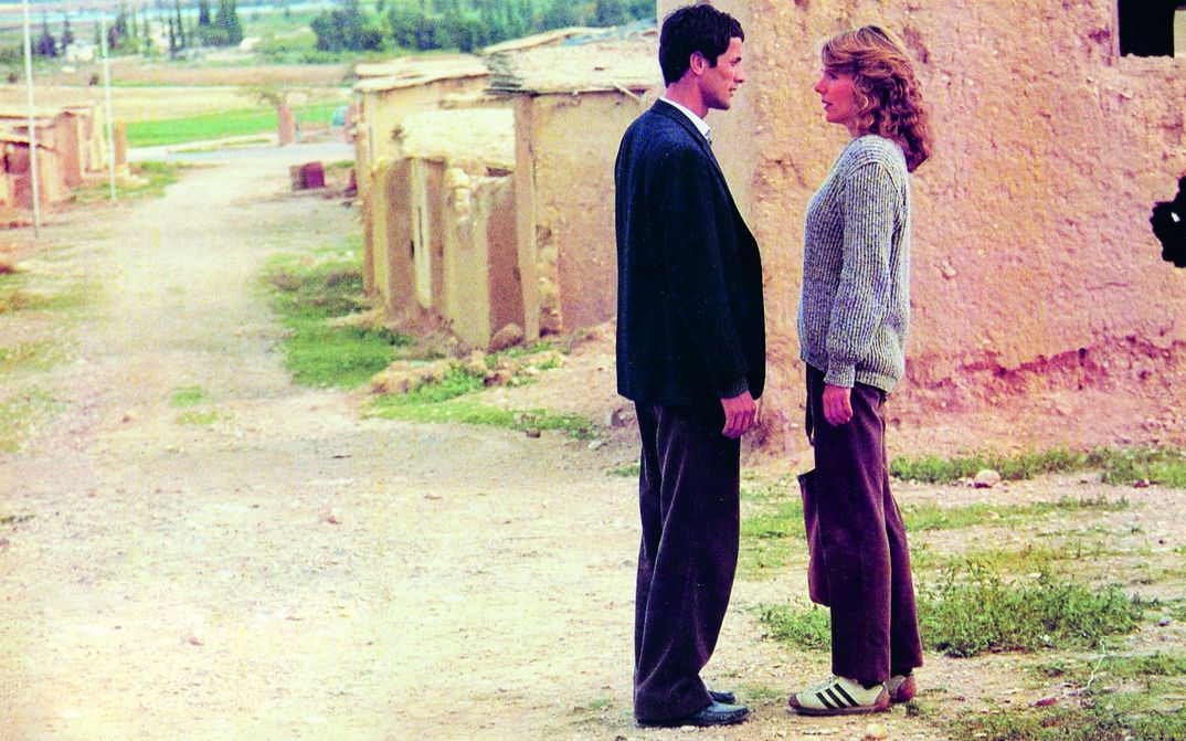 Filmstill aus HANNA K.: Am Rande einer bescheidenen Siedlung stehen ein Mann und eine Frau und blicken sich an.