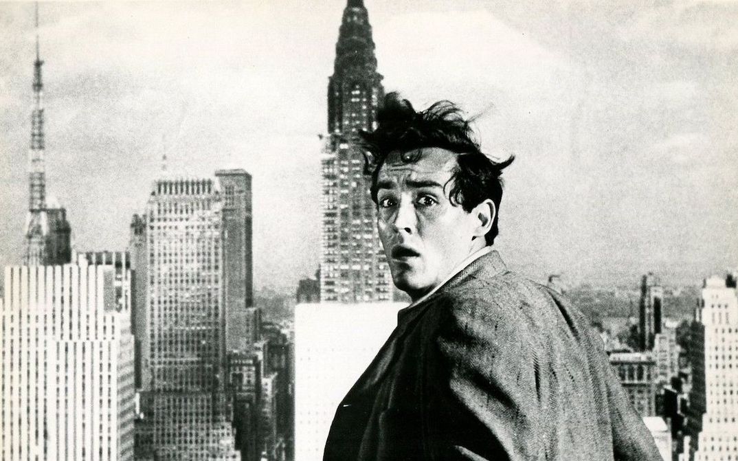Filmstill aus THE GLASS WALL: Ein Mann dreht sich mit erschrecktem Gesichtsausdruck zur Kamera um. Hinter ihm sind die Wolkenkratzer New Yorks zu sehen.