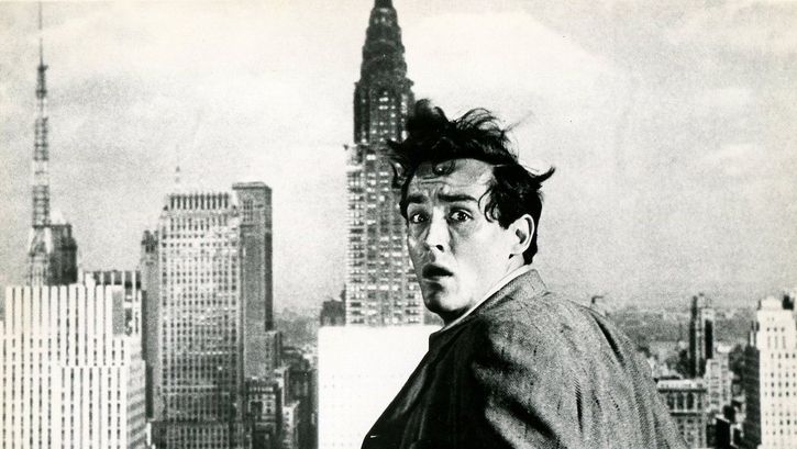 Film still from THE GLASS WALL: A man turns to the camera with a frightened expression on his face. The skyscrapers of New York can be seen behind him.