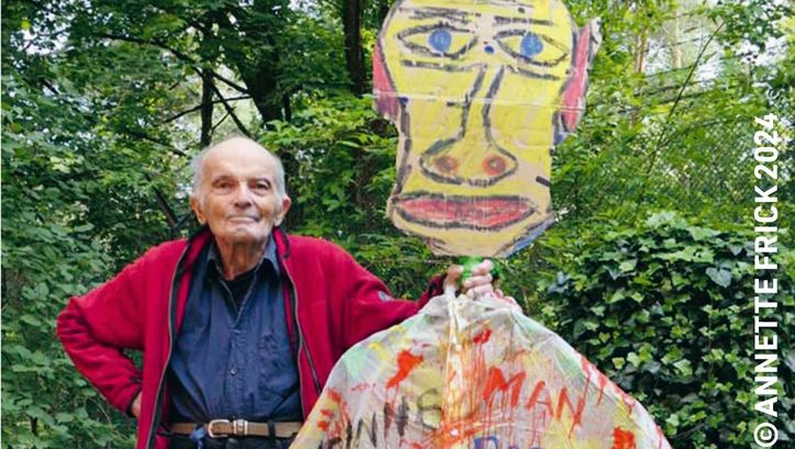 Filmstill aus DAS GROSSE UND DAS KLEINE TOHUWABOHU: Der Filmemacher Wilhelm Hein steht neben einer mannsgroßen Figur mit einem Kopf aus Karton und und einem bunt beschmierten Hemd.