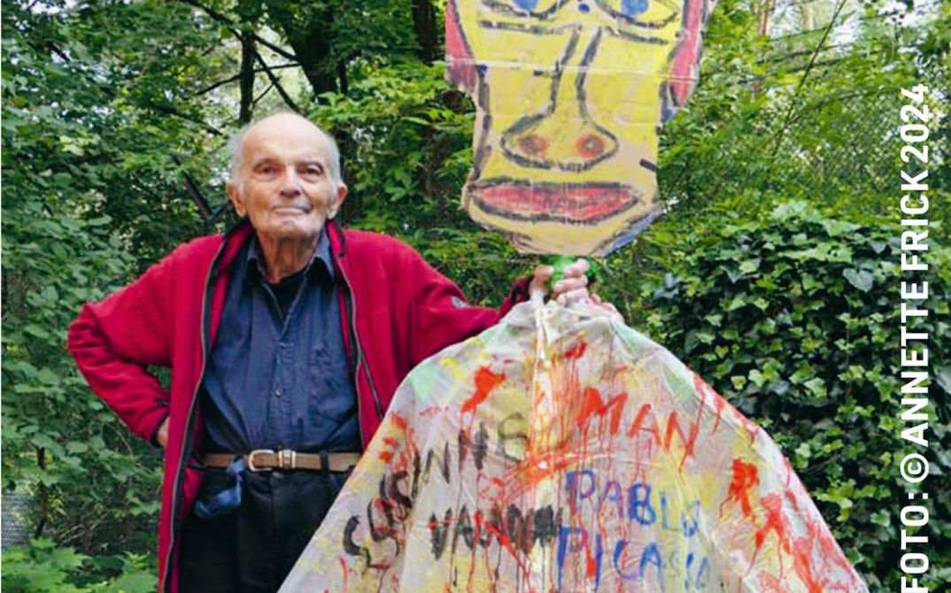 Filmstill aus DAS GROSSE UND DAS KLEINE TOHUWABOHU: Der Filmemacher Wilhelm Hein steht neben einer mannsgroßen Figur mit einem Kopf aus Karton und und einem bunt beschmierten Hemd.