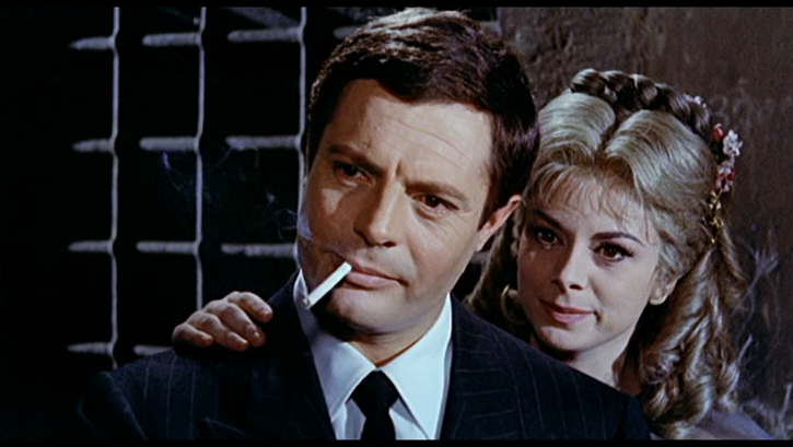 Film still from FANTASMI A ROMA: A man with a cigarette in his mouth. A woman stands behind him and puts a hand on his shoulder.