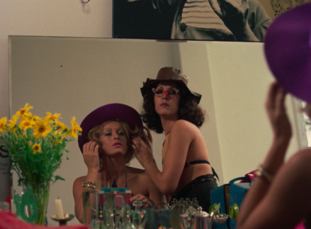 Film still from THE MAN I LOVED: Two women in beachwear and hats look at themselves in a mirror.
