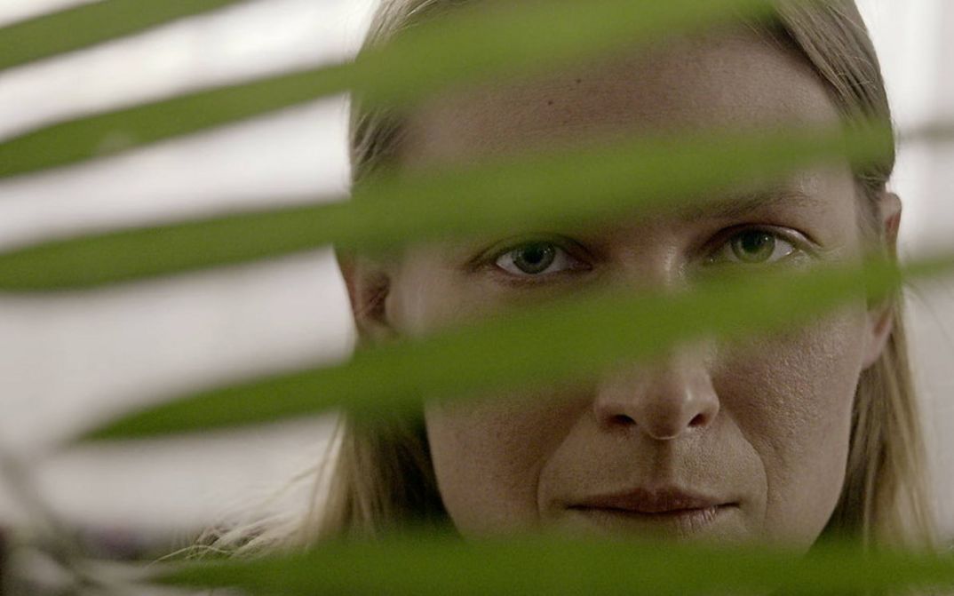 Still from the film „We Haven’t Lost Our Way“  by Anka and Wilhelm Sasnal. A woman peeks through the leaf of a plant. 