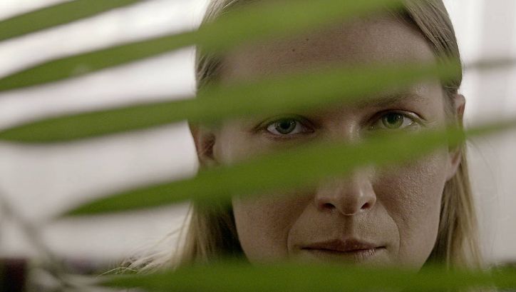 Still from the film „We Haven’t Lost Our Way“  by Anka and Wilhelm Sasnal. A woman peeks through the leaf of a plant. 