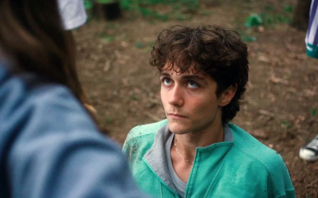 Junger Mann liegt auf erdigem Boden und blickt zu stehender Person auf.