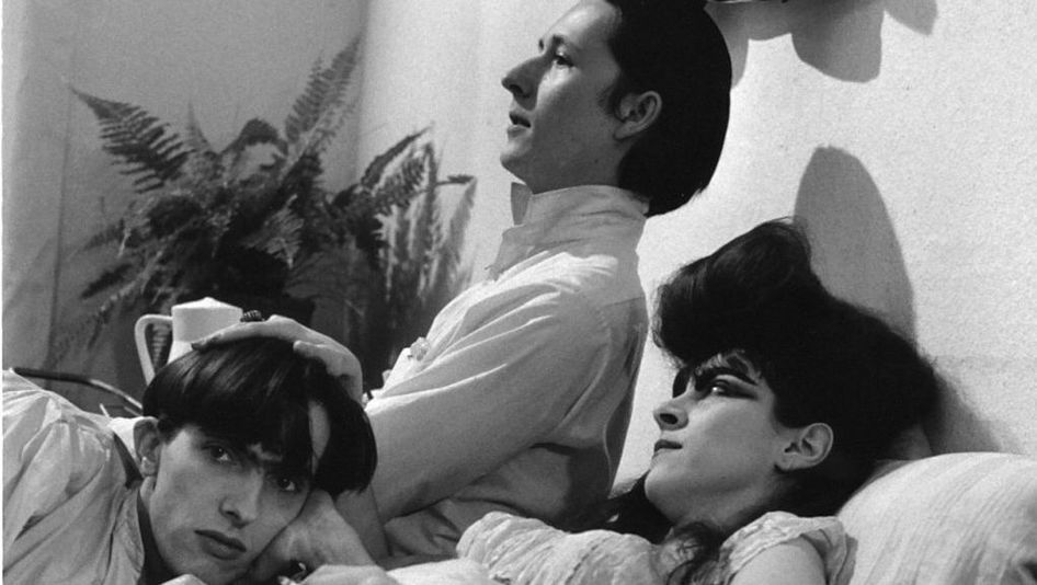 Filmstill aus TAGEDIEBE: Drei junge Menschen, zwei Männer und eine Frau mit einer auffälligen Frisur, liegen angezogen in einem Bett.