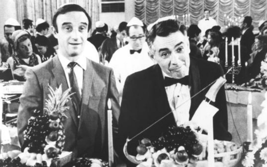 Film still from THE PLOT AGAINST HARRY: Two men at a party are standing in front of a richly laid table. 