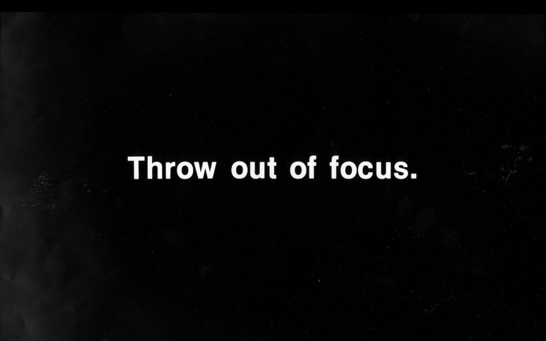 Film still from PROJECTION INSTRUCIONS: In white lettering on a black background it says: Throw out of focus.
