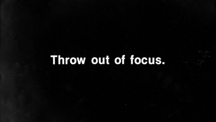 Film still from PROJECTION INSTRUCIONS: In white lettering on a black background it says: Throw out of focus.