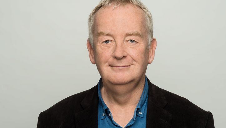 Porträtbild von Ralf Schenk. Er trägt ein Jacket und blaues Hemd und lächelt in die Kamera.