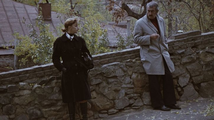 Film still from SOME INTERVIEWS ON PERSONAL MATTERS: A man and a woman stand leaning against a wall on the street and look at each other.