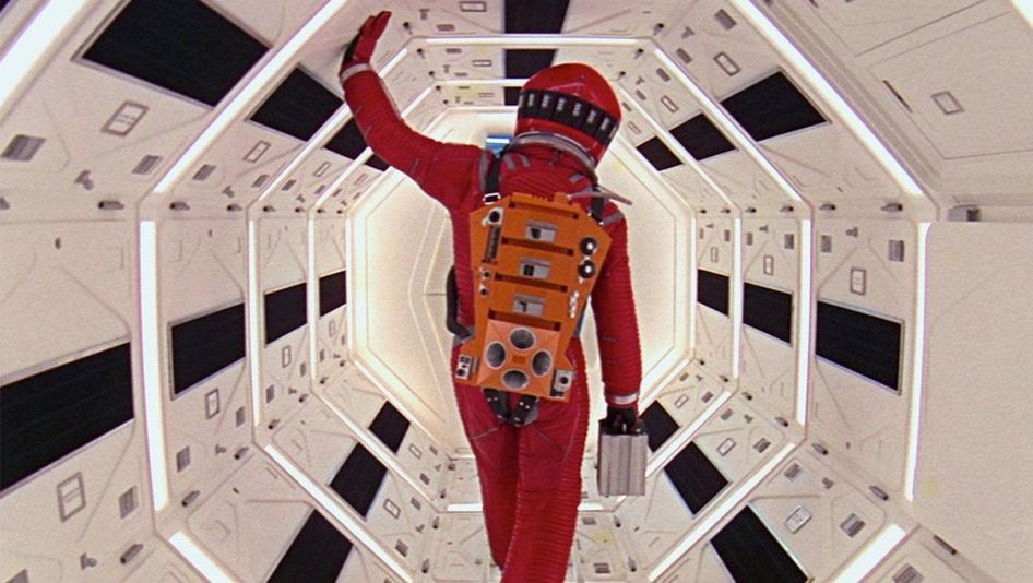Filmstill aus 2001: Ein Astronaut in einem roten Raumanzug geht durch einen engen Korridor in einem Raumschiff.
