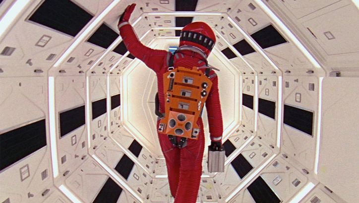 Filmstill aus 2001: Ein Astronaut in einem roten Raumanzug geht durch einen engen Korridor in einem Raumschiff.