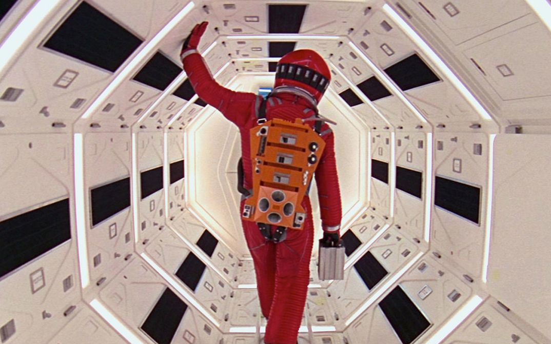 Filmstill aus 2001: Ein Astronaut in einem roten Raumanzug geht durch einen engen Korridor in einem Raumschiff.