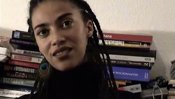 Still from the film "The Maji-Maji Readings" by Ricardo Barcallo. Close up of a women sitting in front of books