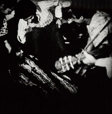 Black and white image of a group of people making music and dancing. The picture was taken from above and shows the people in motion.