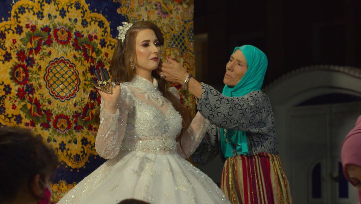 Film still from MACHTAT: An older woman with a turquoise headscarf arranges the hair of a bride.