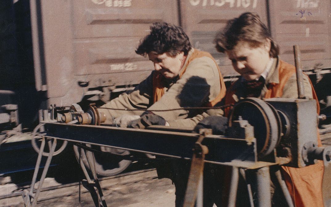 Film still from ORANGE VESTS: Two female workers in orange vests at work on a railroad track.