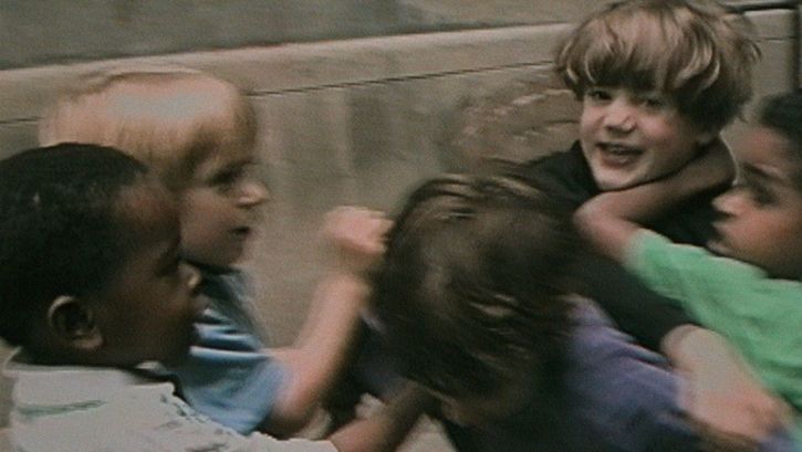 Film still from RÉCRÉATIONS: A group of children in a playful fight.