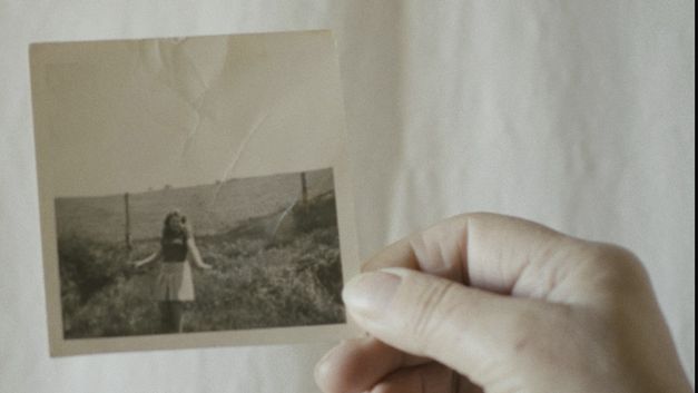 Film still from CANONE EFFIMERO by Gianluca De Serio and Massimiliano De Serio. The image shows a close-up of a black and white photograph held by a hand.
