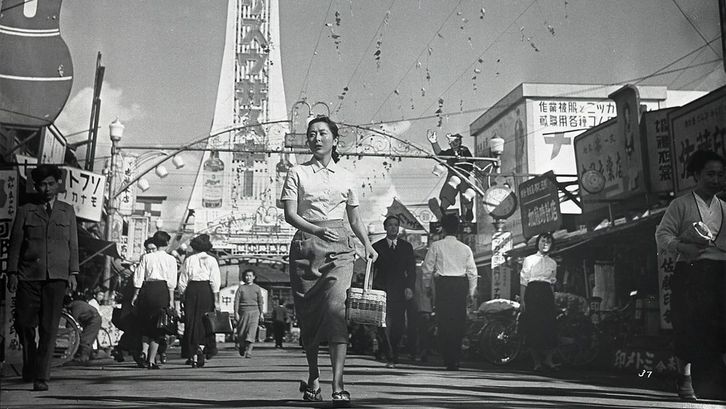 Film still from CHIBUSA YO EIEN NARE: A woman in the midst of a busy street scene.