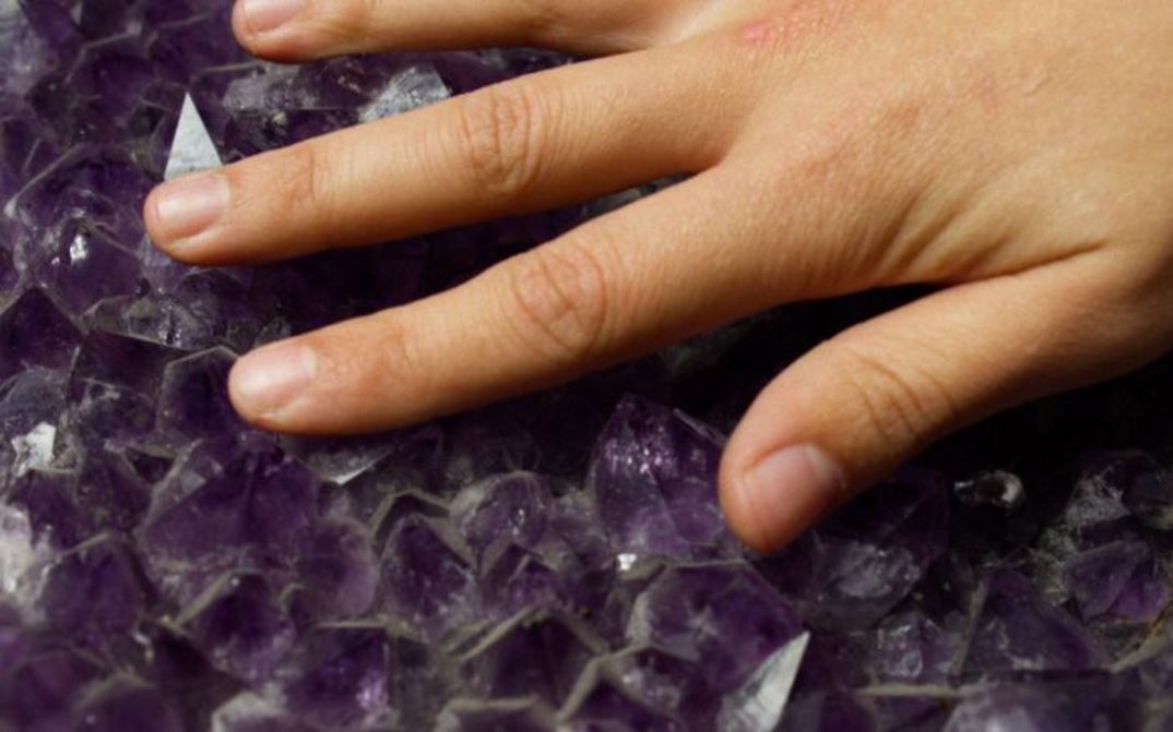 Hand berührt violette Kristalle mit scharfkantiger, unregelmäßiger Oberfläche.