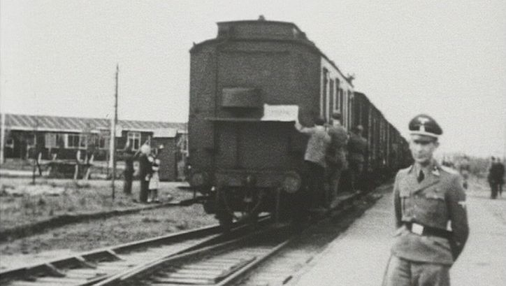 Film still from AUFSCHUB: You can see a historical photograph. An SS man stands in front of a departing train, other people can be seen in the background.