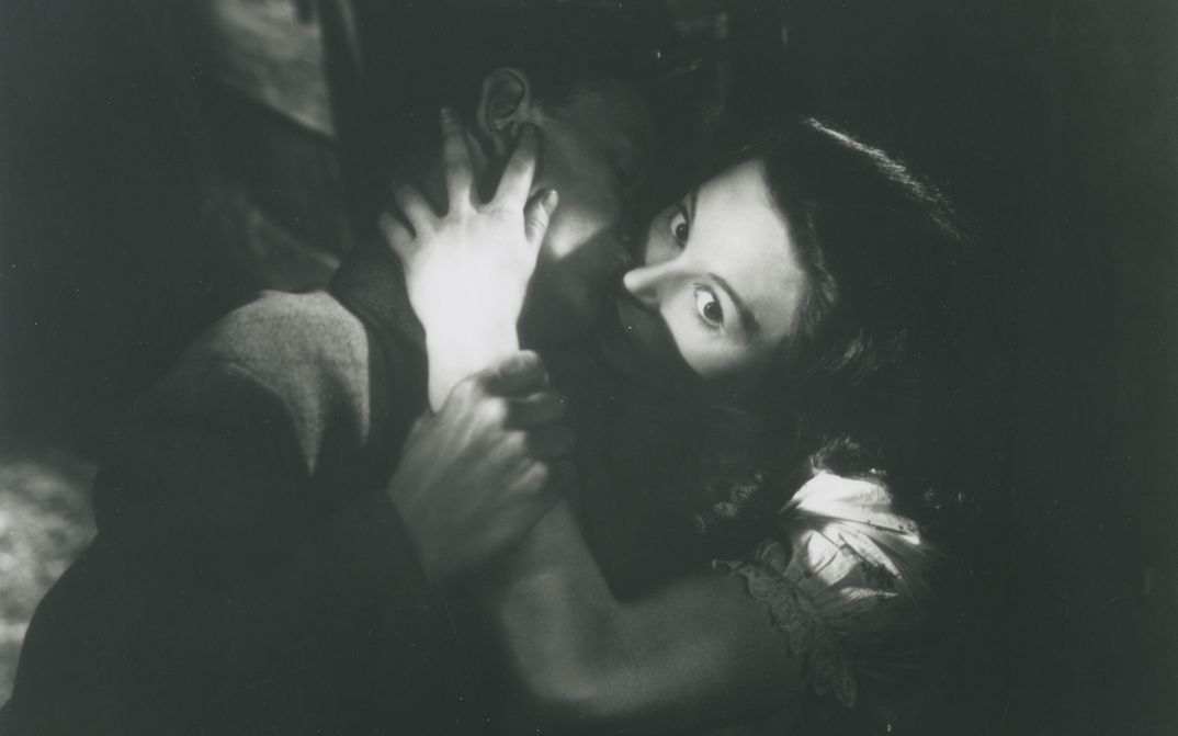 Filmstill aus DAUGHTER OF DARKNESS: Ein junges Paar in einer Umarmung. Der Hintergrund ist dunkel, das Bild hat starke Hell-Dunkel-Kontraste.