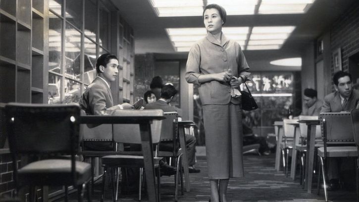 Film still from KOIBUMI: A woman stands in a pub and looks around searchingly.